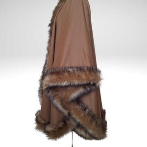 May include: A brown cape with faux fur trim. The cape is displayed on a metal stand against a white background. The faux fur trim is a mix of brown and black.