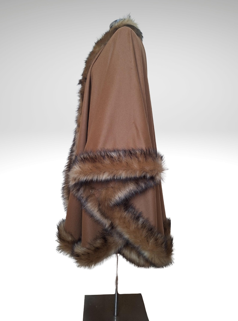 May include: A brown cape with faux fur trim. The cape is displayed on a metal stand against a white background. The faux fur trim is a mix of brown and black.