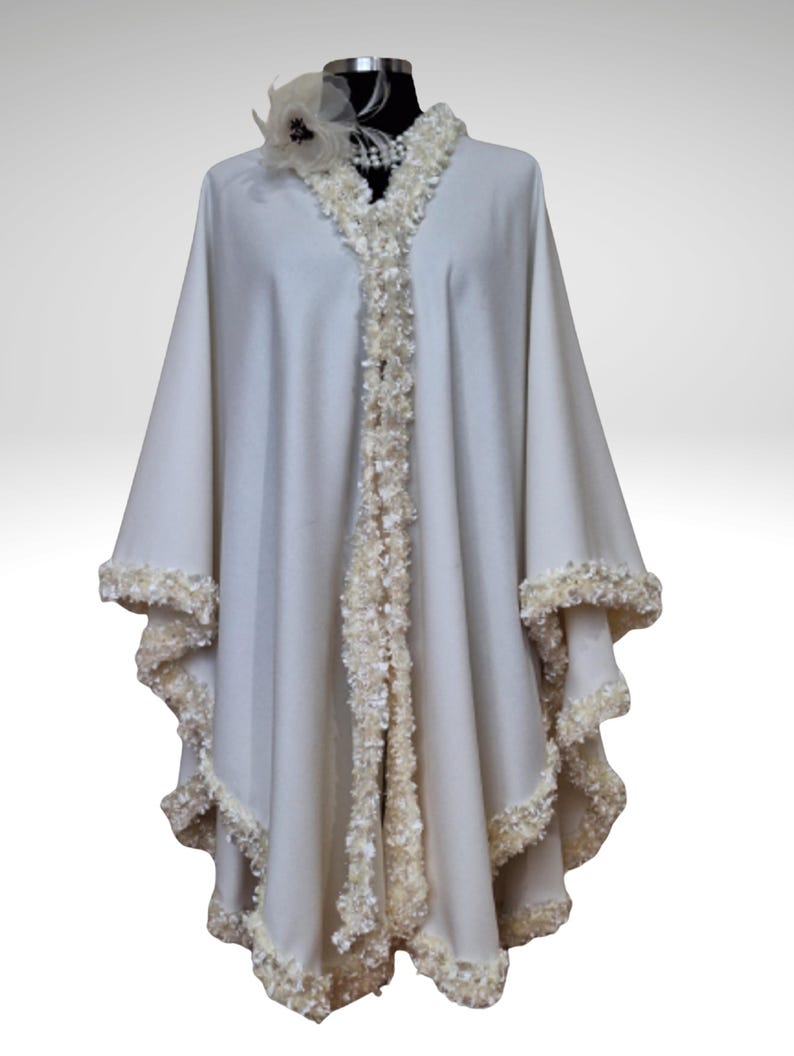 Off-white wedding cashmere cape with lavish handmade trim, featuring intricate soutache and pearl details along the front edges. Flowing vintage-inspired silhouette displayed on a mannequin, perfect for bridal  weddings.