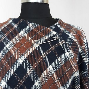 K&ouml;nnte beinhalten: Ein braunes, wei&szlig;es und blaues kariertes Poncho mit einer Sicherheitsnadel zum Verschlie&szlig;en.