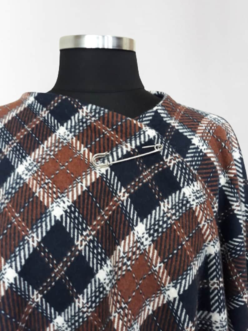 K&ouml;nnte beinhalten: Ein braunes, wei&szlig;es und blaues kariertes Poncho mit einer Sicherheitsnadel zum Verschlie&szlig;en.