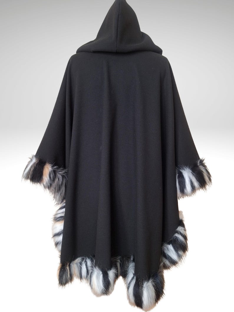 May include: A black hooded cape with faux fur trim. The cape features a hood and is trimmed with black, white, and tan faux fur along the edges of the sleeves and bottom hem. The cape is made of a soft, flowing fabric.