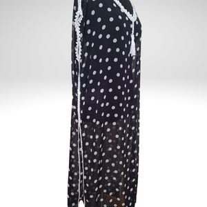 May include: A black and white polka dot dress with white lace trim and a tassel. The dress is displayed on a mannequin. The dress has a V-neckline and long sleeves. The dress is made of a lightweight fabric.