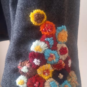 May include: A gray wool jacket with a colorful embroidered floral design on the sleeve. The flowers are made of yarn and are in shades of red, yellow, blue, green, and brown.