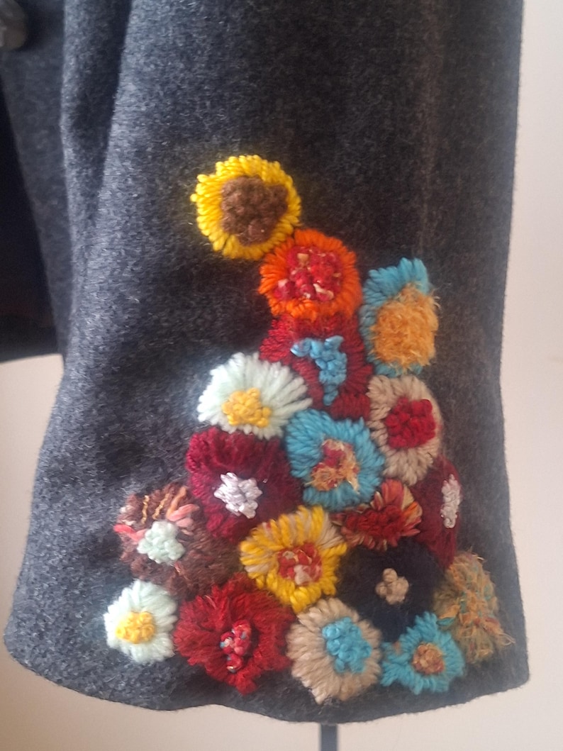 May include: A gray wool jacket with a colorful embroidered floral design on the sleeve. The flowers are made of yarn and are in shades of red, yellow, blue, green, and brown.