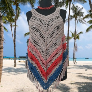 May include: A handmade crochet top in a neutral beige color with a chevron pattern. The bottom features stripes of pink, red, and blue, with fringe. A coral-colored necklace is around the mannequin's neck. The background is a beach scene with palm trees.