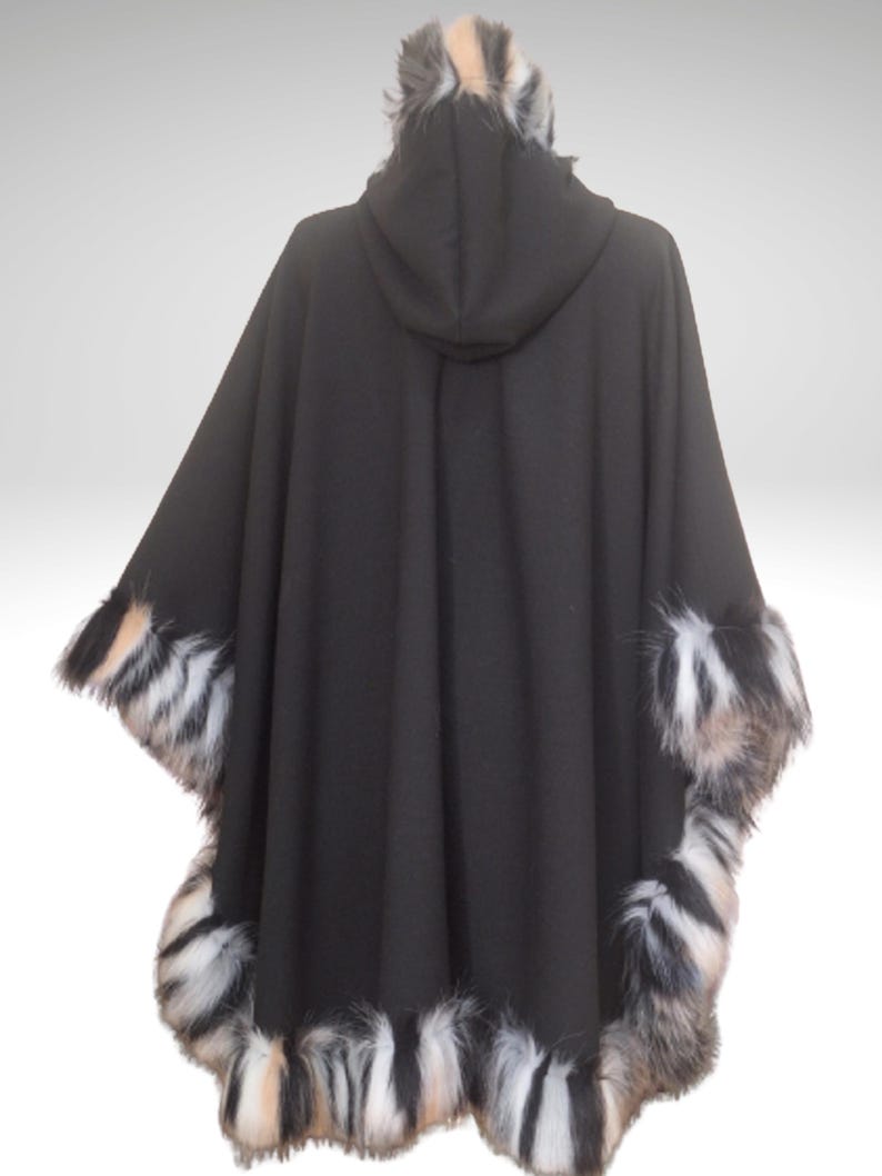 May include: A black hooded cape with faux fur trim. The cape features a hood and is trimmed with a mix of black, white, and tan faux fur along the edges and hood. The cape is displayed against a white background.