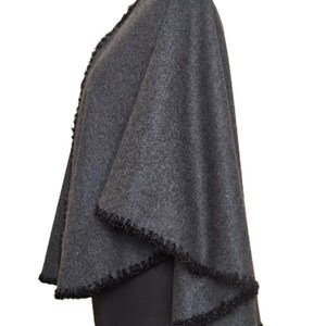 May include: A gray wool cape with a black fringe trim. The cape is draped over a dress form.