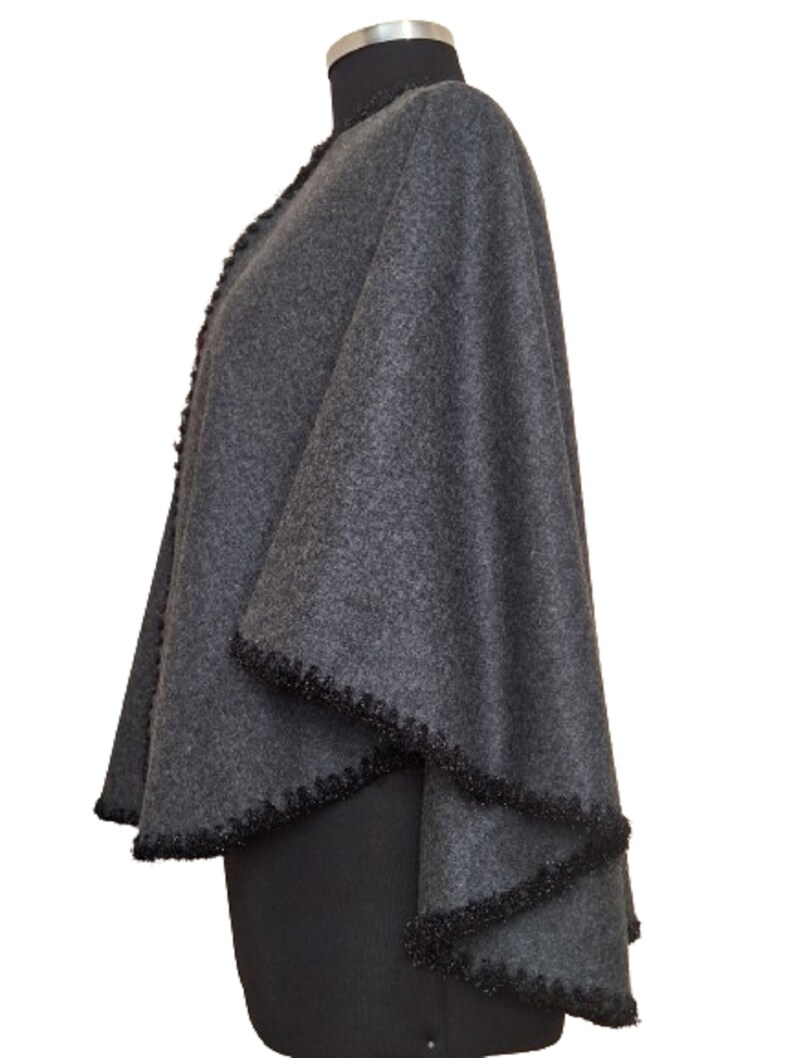 May include: A gray wool cape with a black fringe trim. The cape is draped over a dress form.