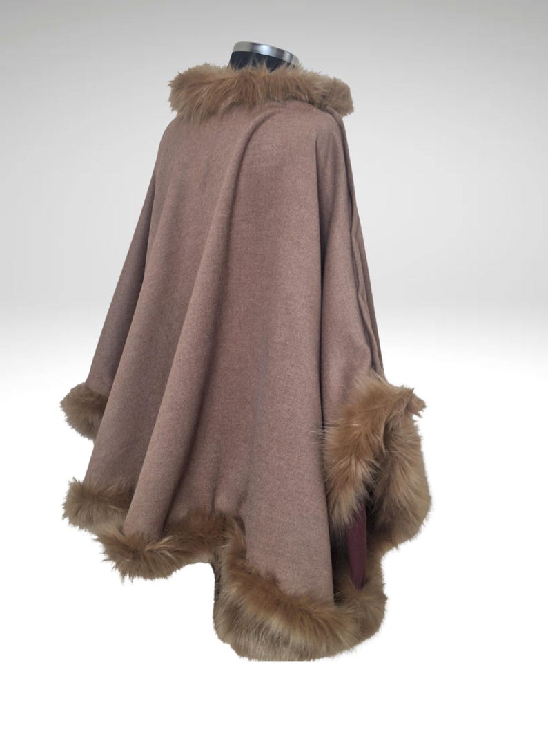 May include: A brown cape with faux fur trim around the collar and cuffs. The cape is displayed on a mannequin and has a flowing design. The faux fur is a lighter shade of brown than the cape.