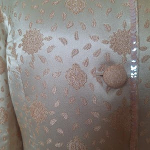 May include: A light green jacket with a floral pattern and sequins. The jacket has a button closure and a sequined trim.