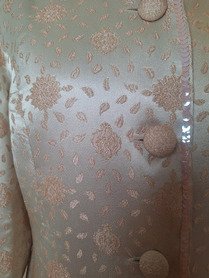 May include: A light green jacket with a floral pattern and sequins. The jacket has a button closure and a sequined trim.