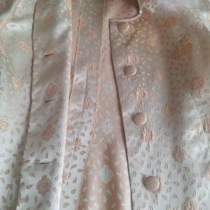 May include: A white and pink patterned jacket with a floral design. The jacket has a button closure and a collar.