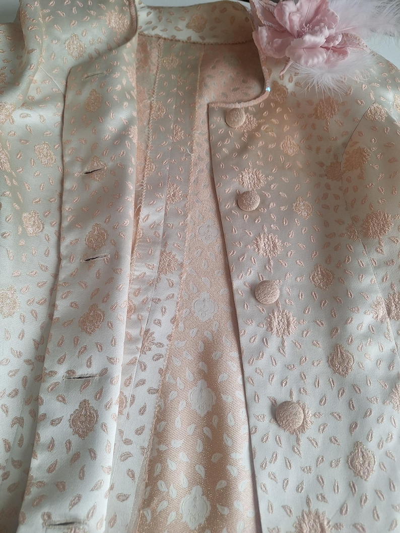 May include: A white and pink patterned jacket with a floral design. The jacket has a button closure and a collar.