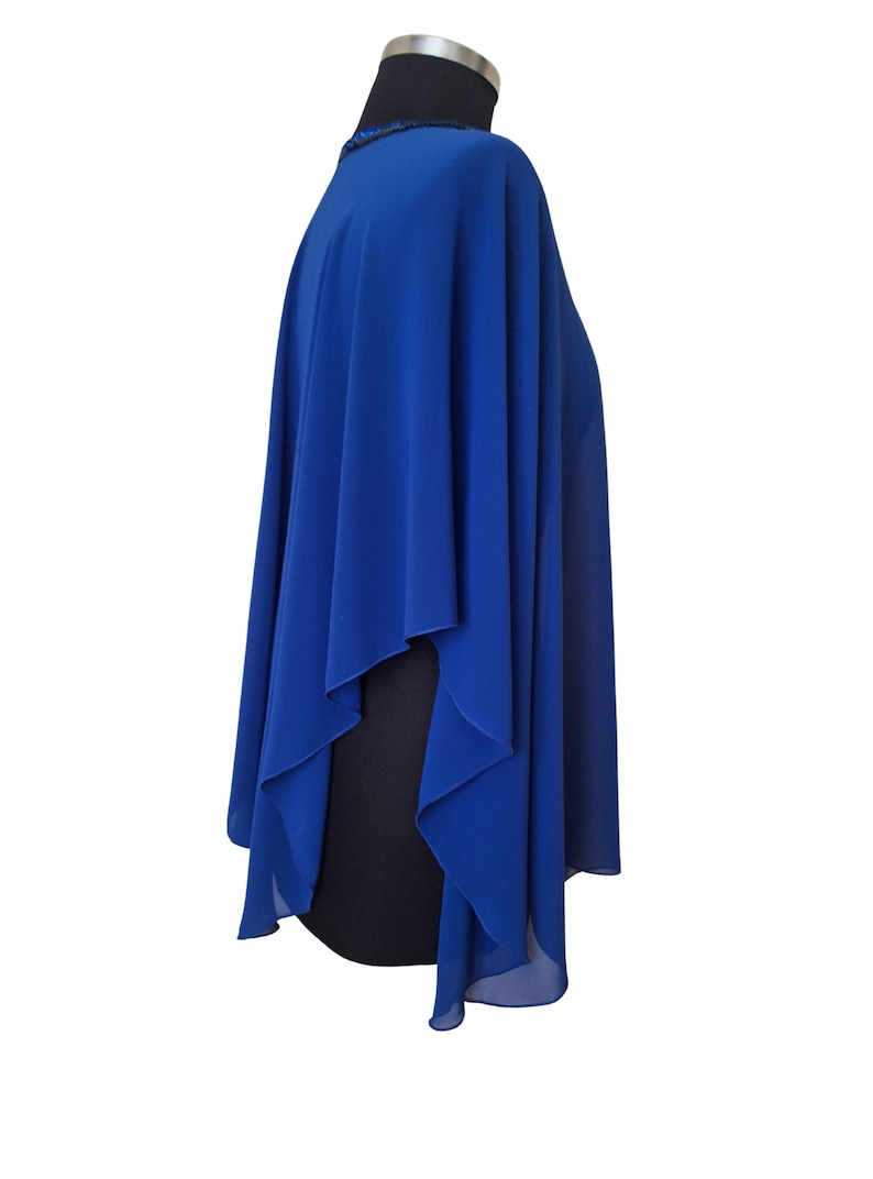 May include: A royal blue cape-style garment with a flowing design. The cape is draped over a black form, showcasing its shape and texture. The neckline appears to have a subtle beaded detail.
