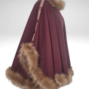 May include: A burgundy cape with faux fur trim and collar. The cape has a tan accent strip with brown buttons. The faux fur is light brown. The cape is a winter garment.