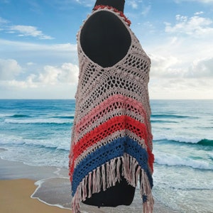 May include: A handmade, open-weave crochet top in a sleeveless design. The top features a V-neck and a color block pattern with stripes of pink, red, and blue. The bottom edge has long fringe. A coral-colored necklace is around the mannequin's neck.