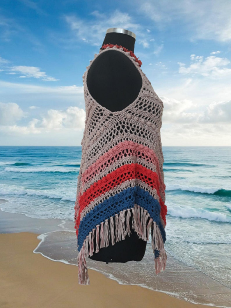 May include: A handmade, open-weave crochet top in a sleeveless design. The top features a V-neck and a color block pattern with stripes of pink, red, and blue. The bottom edge has long fringe. A coral-colored necklace is around the mannequin's neck.