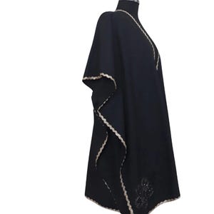 A black linen garment with gold trim and a subtle embroidered design on the lower left, displayed on a mannequin from the right side.