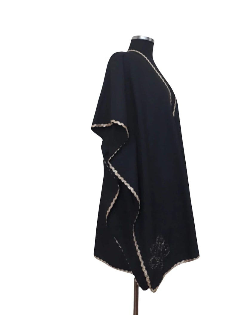 A black linen garment with gold trim and a subtle embroidered design on the lower left, displayed on a mannequin from the right side.