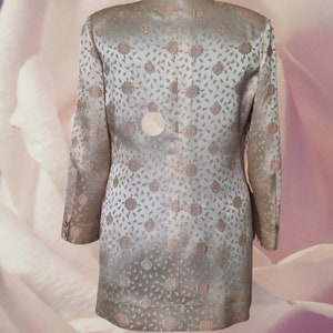 May include: A light beige blazer with a floral pattern. The blazer has a long sleeve and a button closure.