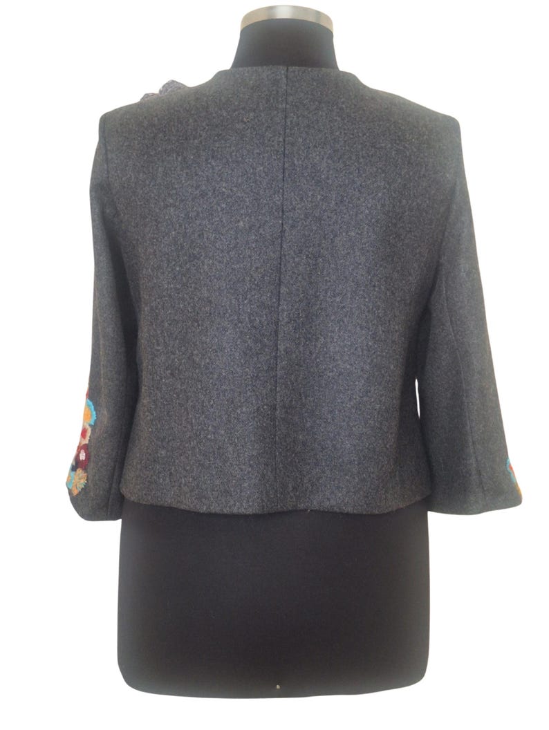 May include: A gray wool jacket with colorful embroidered details on the sleeves. The jacket has a round neckline and a cropped length.