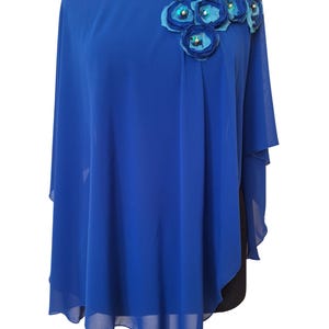 May include: A royal blue cape-style top with a round neckline embellished with sequins. The shoulder is adorned with fabric flowers in shades of blue and teal, with pearl and sequin accents. The fabric drapes loosely.