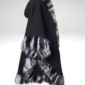 May include: A black hooded cape with faux fur trim in shades of gray, white, and brown. The cape is made of a soft, dark fabric and features fur accents around the hood and edges, creating a luxurious look.