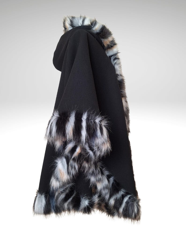 May include: A black hooded cape with faux fur trim in shades of gray, white, and brown. The cape is made of a soft, dark fabric and features fur accents around the hood and edges, creating a luxurious look.