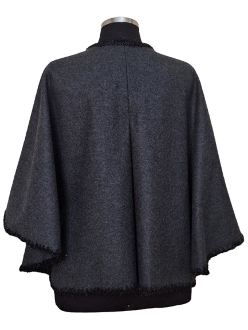 May include: A charcoal gray wool poncho with a black beaded trim around the neckline and edges.