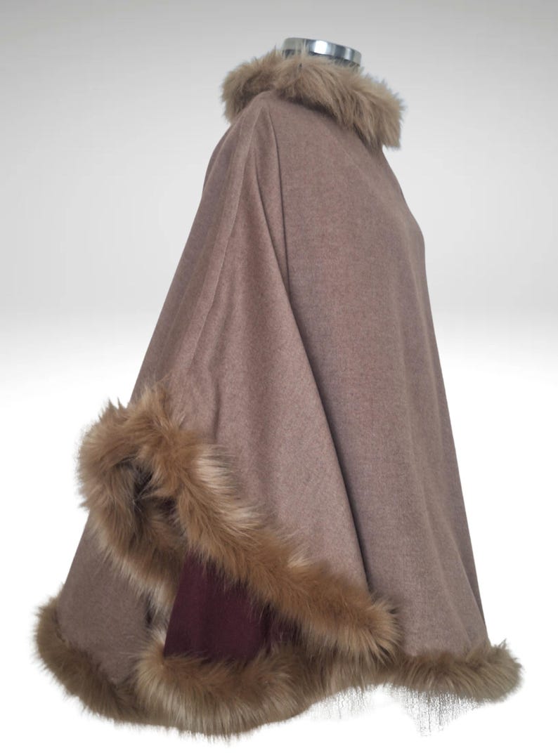 May include: A brown cape with faux fur trim around the collar and edges. The cape is made of a soft material and has a burgundy accent on the inside. The faux fur is a light brown colour.