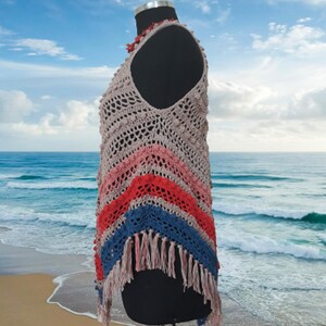 May include: A handmade crochet top in a variety of colors, including beige, pink, red, and blue. The top features a fringed hemline and is displayed on a black mannequin. The crochet design has a textured, open weave.