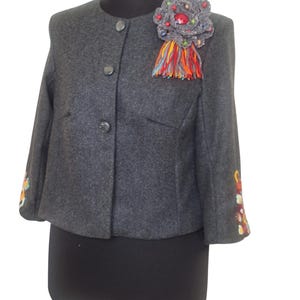 Handmade cropped wool alpaca jacket featuring intricate hand-embroidered floral details on the sleeves and a unique artisan brooch, showcasing exceptional craftsmanship.