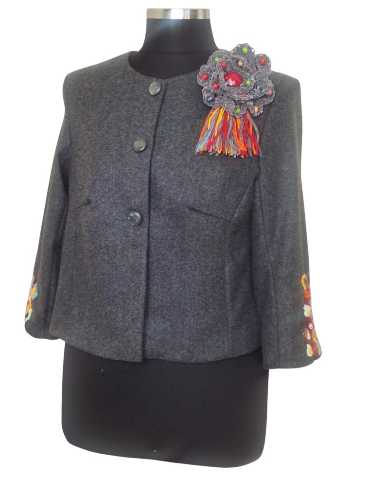 Handmade cropped wool alpaca jacket featuring intricate hand-embroidered floral details on the sleeves and a unique artisan brooch, showcasing exceptional craftsmanship.