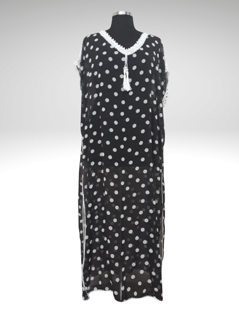 May include: Black and white polka dot dress with white crochet trim and a tassel. The dress is displayed on a mannequin. The dress has a V-neckline and a loose, flowing silhouette. The dress is floor-length.