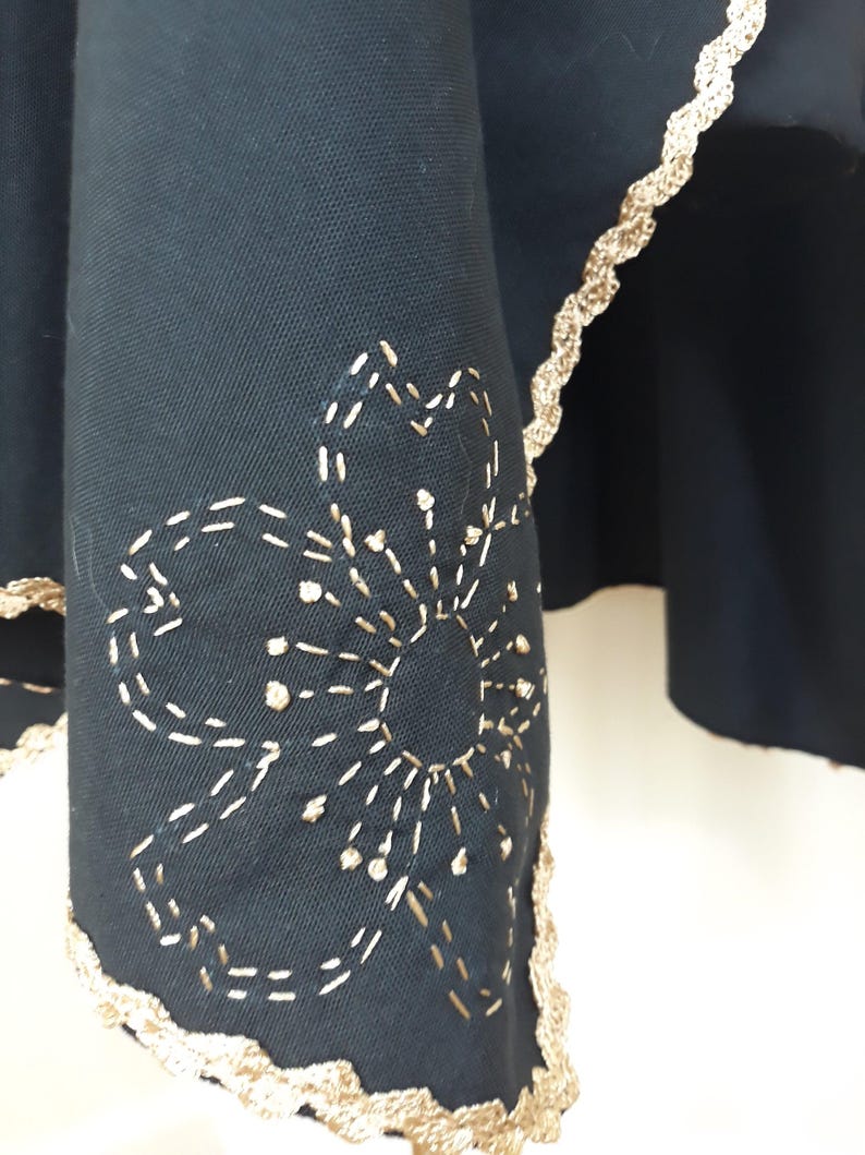 A close-up of the bottom edge of a black linen garment, showing gold trim and a gold embroidered flower design.