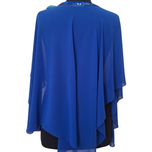 May include: Royal blue cape-style shawl with a flowing design. The shawl features a sequined neckline and a decorative accent on the shoulder. The fabric drapes elegantly, creating a sophisticated look. Perfect for formal events or adding a touch of elegance to any outfit.