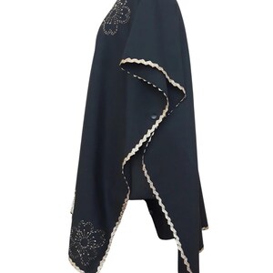 A black linen garment with gold trim and two gold embroidered flower designs, displayed on a mannequin from the left side.