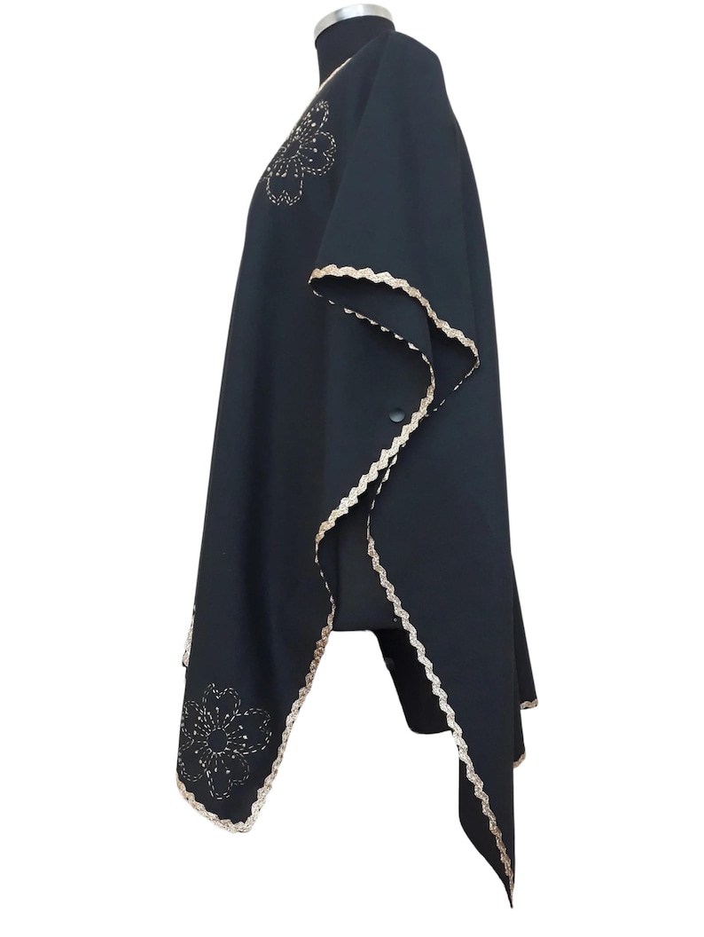 A black linen garment with gold trim and two gold embroidered flower designs, displayed on a mannequin from the left side.