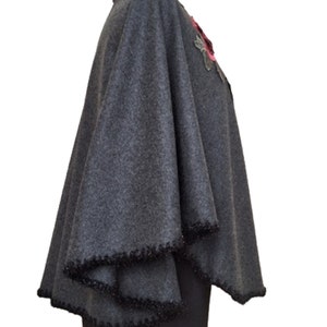 May include: A gray wool poncho with a black beaded trim and a pink and green floral embellishment.