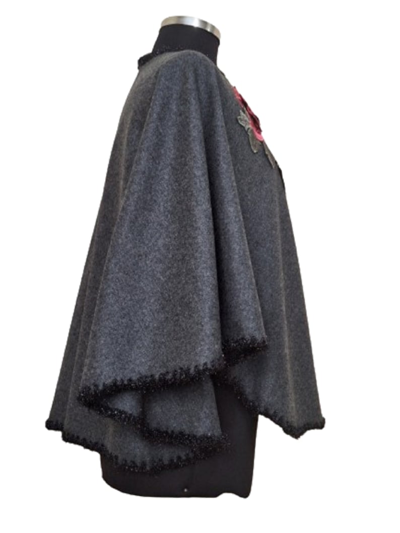 May include: A gray wool poncho with a black beaded trim and a pink and green floral embellishment.
