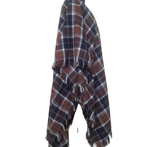 K&ouml;nnte beinhalten: Ein braunes, schwarzes und wei&szlig;es kariertes Poncho mit Fransenbesatz. Das Poncho ist &uuml;ber einen Mannequin drapiert.