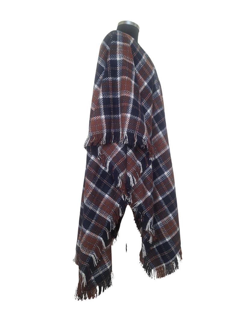 K&ouml;nnte beinhalten: Ein braunes, schwarzes und wei&szlig;es kariertes Poncho mit Fransenbesatz. Das Poncho ist &uuml;ber einen Mannequin drapiert.