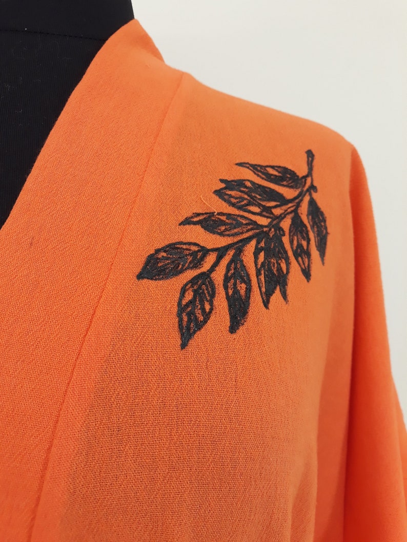 Puede incluir: Kimono naranja con un dise&ntilde;o de hoja bordada en negro en el hombro.
