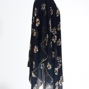 Puede incluir: Kimono negro de gasa transparente con estampado floral en tonos amarillos, rojos y verdes. El kimono tiene una silueta larga y fluida y un dobladillo ligeramente asim&eacute;trico.