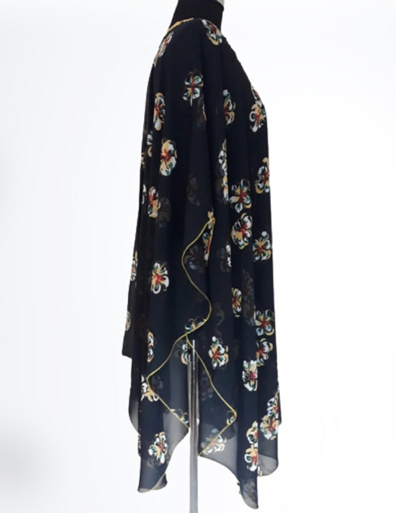 Puede incluir: Kimono negro de gasa transparente con estampado floral en tonos amarillos, rojos y verdes. El kimono tiene una silueta larga y fluida y un dobladillo ligeramente asim&eacute;trico.