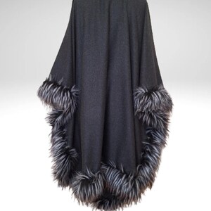 May include: A dark grey cape with a faux fur trim in shades of grey and black. The cape has a high collar and a flowing design, suitable for outerwear. The faux fur trim is around the collar and the edges of the cape.