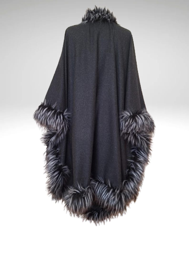May include: A dark grey cape with a faux fur trim in shades of grey and black. The cape has a high collar and a flowing design, suitable for outerwear. The faux fur trim is around the collar and the edges of the cape.