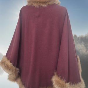 May include: A burgundy poncho with a faux fur collar and trim. The poncho is made of a soft, warm fabric and is perfect for cold weather.