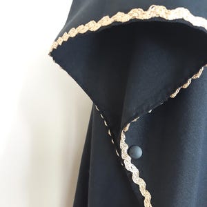 A close-up of a black linen garment with gold trim along the collar and a single gray button closure.